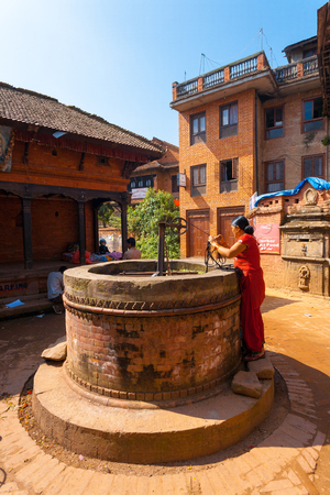 Bhaktapur, Nepal - October 25, 2013: Nepalese woman pulling water from traditional community ground wellのeditorial素材