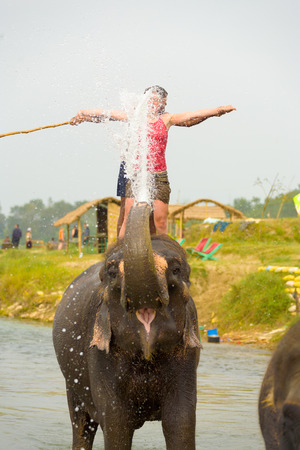 Chitwan, Nepal - December 4, 2007: A female tourist in red enjoying getting splashed by elephant trunk during elephant ride at Chitwan National Parkのeditorial素材
