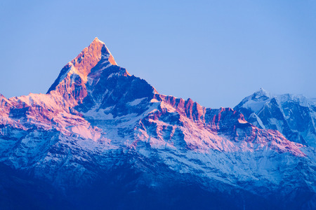 Colorful red glow on the peak of snowy Machapuchare Himalayan mountain peak at dawn sunrise in Nepalの写真素材