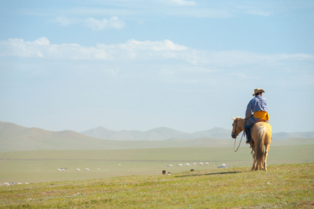 Ulaanbaatar, Mongolia - June 12, 2007: Rear of Mongolian man on horseback in traditional clothes looking at view over a hill on the steppe in the countrysideのeditorial素材