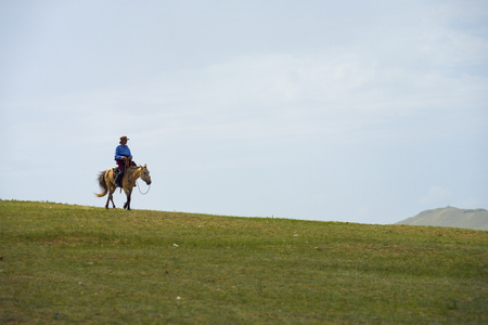 Ulaanbaatar, Mongolia - June 12, 2007: Mongolian man on horseback against a cloudy sky riding horse down a hill on the steppe in the countrysideのeditorial素材