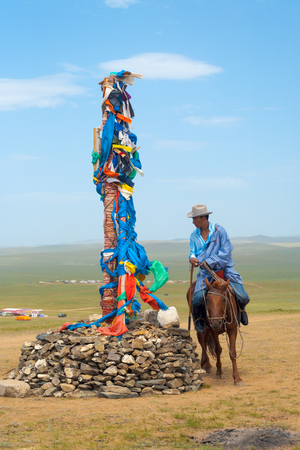 Ulaanbaatar, Mongolia - June 12, 2007: A Mongolian man in traditional clothes riding horse, circumambulating around small stupa and prayer flags on the steppe in rural Mongoliaのeditorial素材