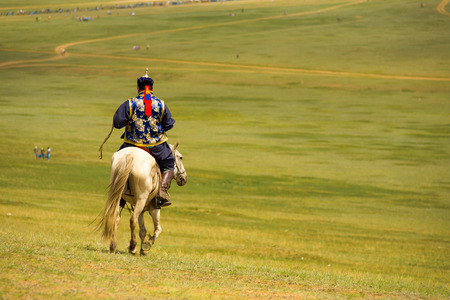 Ulaanbaatar, Mongolia - June 12, 2007: Rear of a Mongolian man in traditional clothes riding his horse downhill on the grassy steppe in rural Mongoliaのeditorial素材