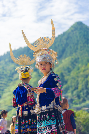 Xijiang, China - September 15, 2007: An ethnic minority Miao woman in traditional festival clothes and silver headdress standing in front of nature background at Miao village in Guizhou, Chinaのeditorial素材