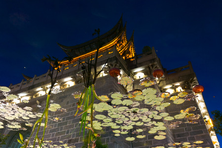 A Chinese style gate with pagoda artisitically reflected in pond water at night in old town Lijiang, Chinaのeditorial素材