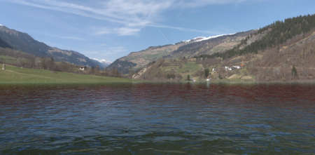 water. Lake at the foot of the mountain. snowcaps. Green meadow and small houses in the forest. beautiful green fields. 3d rendering.の写真素材