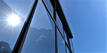 View from below of the glass facade reflecting the bright summer sun in mountains against the blue sky. Suitable illustration for the real estate design magazine. 3d rendering.の写真素材