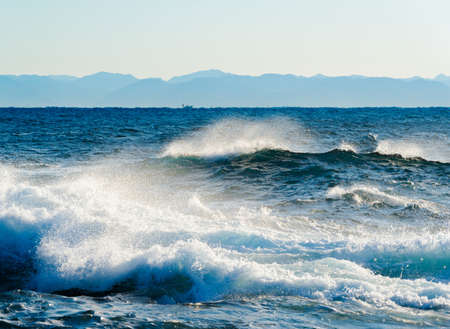 Offshore winds shred the crests of waves pounding the rocky coastline as the morning light catches droplets of ocean spray midair creating a dazzling mist of glistening beads of light.の写真素材