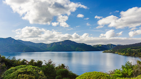 A serene view of Lake Ashi (Ashinoko) from the Benten-no-Hana Tenbodai viewing platform in Onshi Hakone Park, Hakone, Japan. Mt. Mikuni stands prominently in the mid-ground, while on clear days, Mt. Fuji graces the horizon. To the right, the roofline of the historic Ryuguden Honkan hot spring resort hotel emerges through the lush scenery.の写真素材