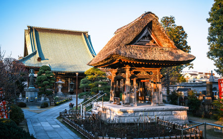 A wooden bell tower in the courtyard of Ryuge-ji Temple, Yokohama, Japan. Built with stout corner pillars and an open design, it houses a large bell hung from a central beam. This style dates back to the 13th century. The thatched roof, once common, is now a rarity, with clay tiles more prevalent today.の写真素材