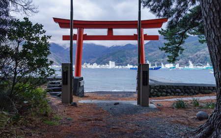 A striking vermilion torii gate stands at the edge of a slim sandy beach on Cape Mihama, overlooking...