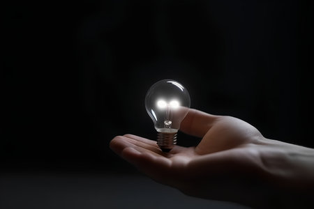 Hand holding a lightbulb on a dark background, energy conceptの素材