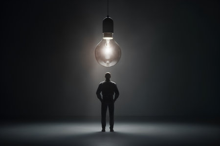 Businessman looking at light bulb above his head on dark background conceptの素材