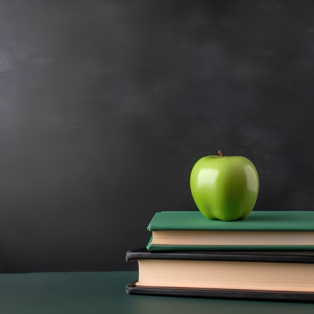 Stack of books and green apple on blackboard background. Back to school concept.の素材