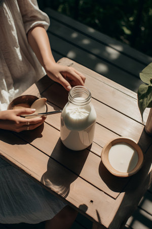woman pouring milk into glass of yogurt on wooden table in summer gardenの素材