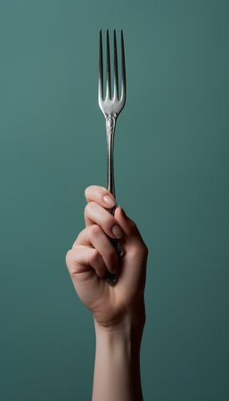Female hand holding a silver fork on a green background. Place for text.の素材