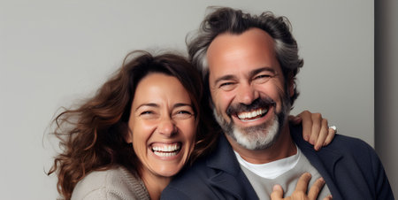 Portrait of a happy mature couple embracing and smiling while standing against grey backgroundの素材