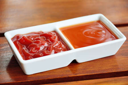 Chilli sauce and tomato sauce in white dish on wooden tableの写真素材