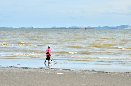 CHONBURI, THAILAND - JULY 15 : Unidentified man walking with metal detector for valuable on 15 July 2013 in the beach of Bangsaen, Chonburi, Thailandのeditorial素材
