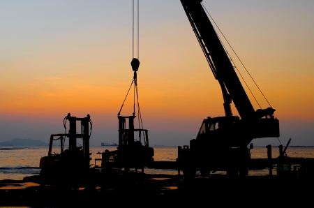 Silhouette crane working at port with sunset sky backgroundの写真素材