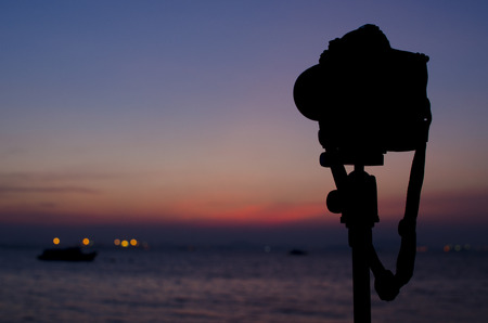 Silhouette of digital camera on tripod with sunset sky at sea blured backgroundの写真素材