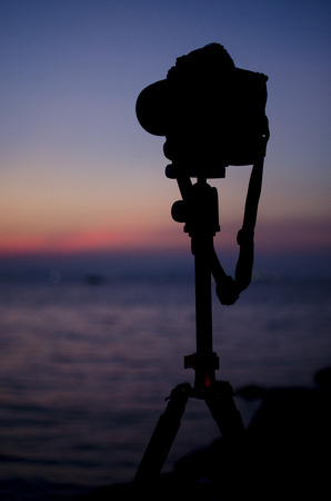 Silhouette of digital camera on tripod with sunset sky at sea blured backgroundの写真素材