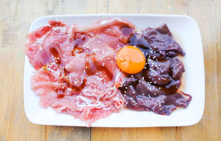 Raw pork and fresh liver with egg in white dish ready for cook in shabu potの写真素材