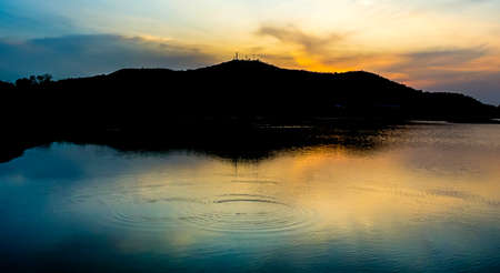 Wave on water surface with silhouette of mountain and dramatic skyの写真素材