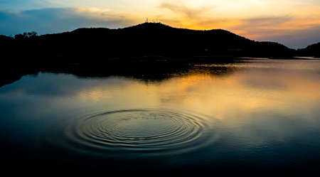 Wave on water surface with silhouette of mountain and dramatic skyの写真素材