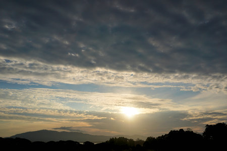 Sun with clouds in sky with mountain silhouette backgroundの写真素材