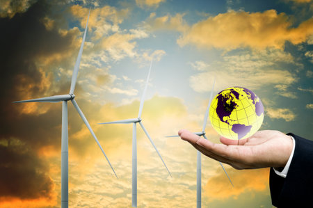 Green energy and sustainable concept, Businessman hand hold the world and wind turbine with sunset sky backgroundの写真素材