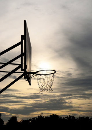 Silhouette of basketball hoop with sunset and clouds backgroundの写真素材