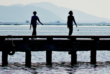 Silhouette of men walking on bridge with island backgroundの写真素材