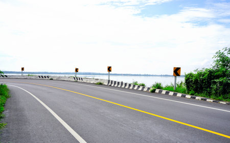 Light traffic on road beside lake with clouds sky backgroundの写真素材