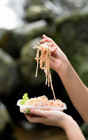 Lunch box at waterfall, Spaghetti ready to eat with woman hand holding fork and lift up