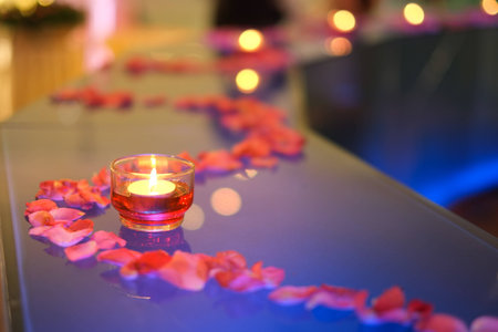 Beautiful romantic red candles with flower petals on white glass backgroundの写真素材