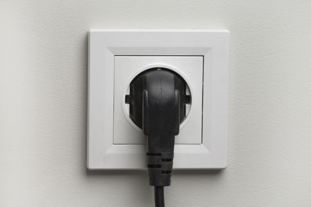 Electric white socket and one plugged in power cord on white wall background.の写真素材