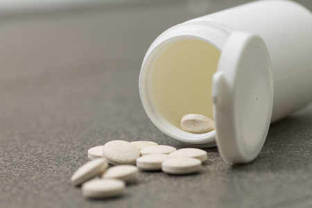 Vitamin pills drugs acid is scattered out of the jar on a black background. Drugs are jumping out of the white jar.の写真素材