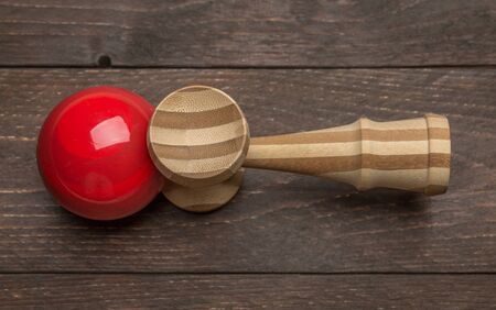 Red kendama laying on the side on a dark wooden rustic background. Traditional japanese toy. Accuracy and agility development. Kids, children, ball gameの写真素材