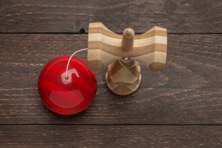 Kendama standing on a dark wooden rustic background red ball is near. Traditional japanese toy. Accuracy and agility development. Kids, children, ball game.の写真素材