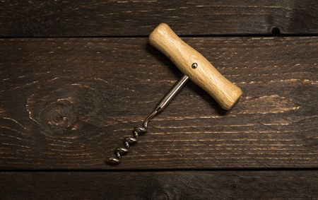 Corkscrew opener for wine cork on dark chocolate wooden background. Bottle-screw to open wine alcohol bottle at rustic vintage brown table.の写真素材