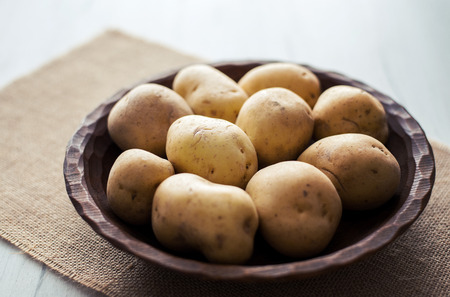 Raw potatoes in rustic wooden plate, on bright background. Organic agriculture & food concept.の写真素材