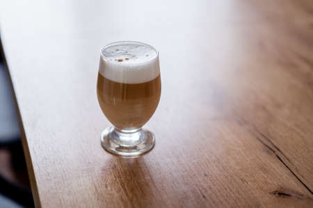 Caffe latte macchiato coffee layered with milk in a high drinking glass on a wooden table.の写真素材