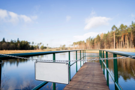 Blank sign on a chain on a wooden bridge over a lakeの写真素材
