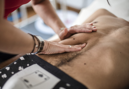 physiotherapist visits a young sportsman who feels pain at abdomenの写真素材