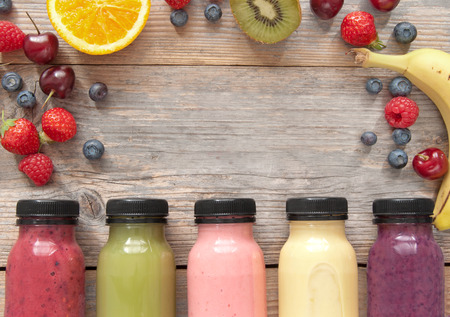 Assorted flavoured smoothie juices in bottles over a wooden background with fruitの写真素材