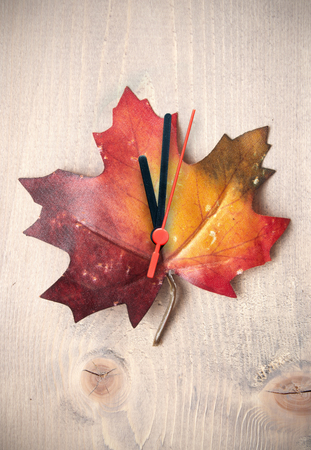 Autumn leaf with clock hands on top of a wooden backgroundの写真素材