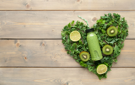 Bottled green smoothie with ingredients in a heart shape over a wooden tableの写真素材
