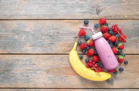 Berry smoothie in a bottle with ingredients on top of a wooden background with spaceの写真素材
