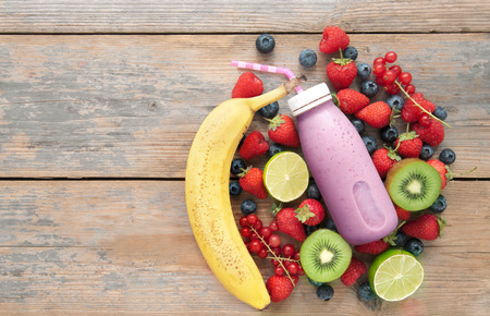 Berry smoothie in a bottle with ingredients on top of a wooden background with spaceの写真素材